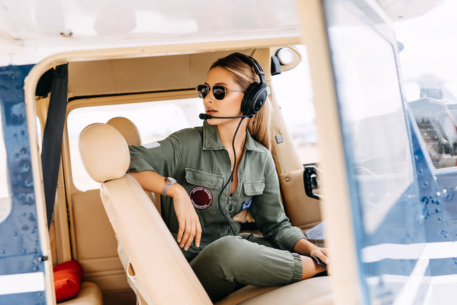 Woman pilot in private airplane cockpit, wearing headset and sunglasses.