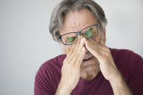 A man wearing glasses rubbing his eyes