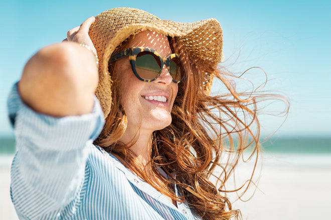 Woman wearing Tory Burch reading sunglasses on the beach.